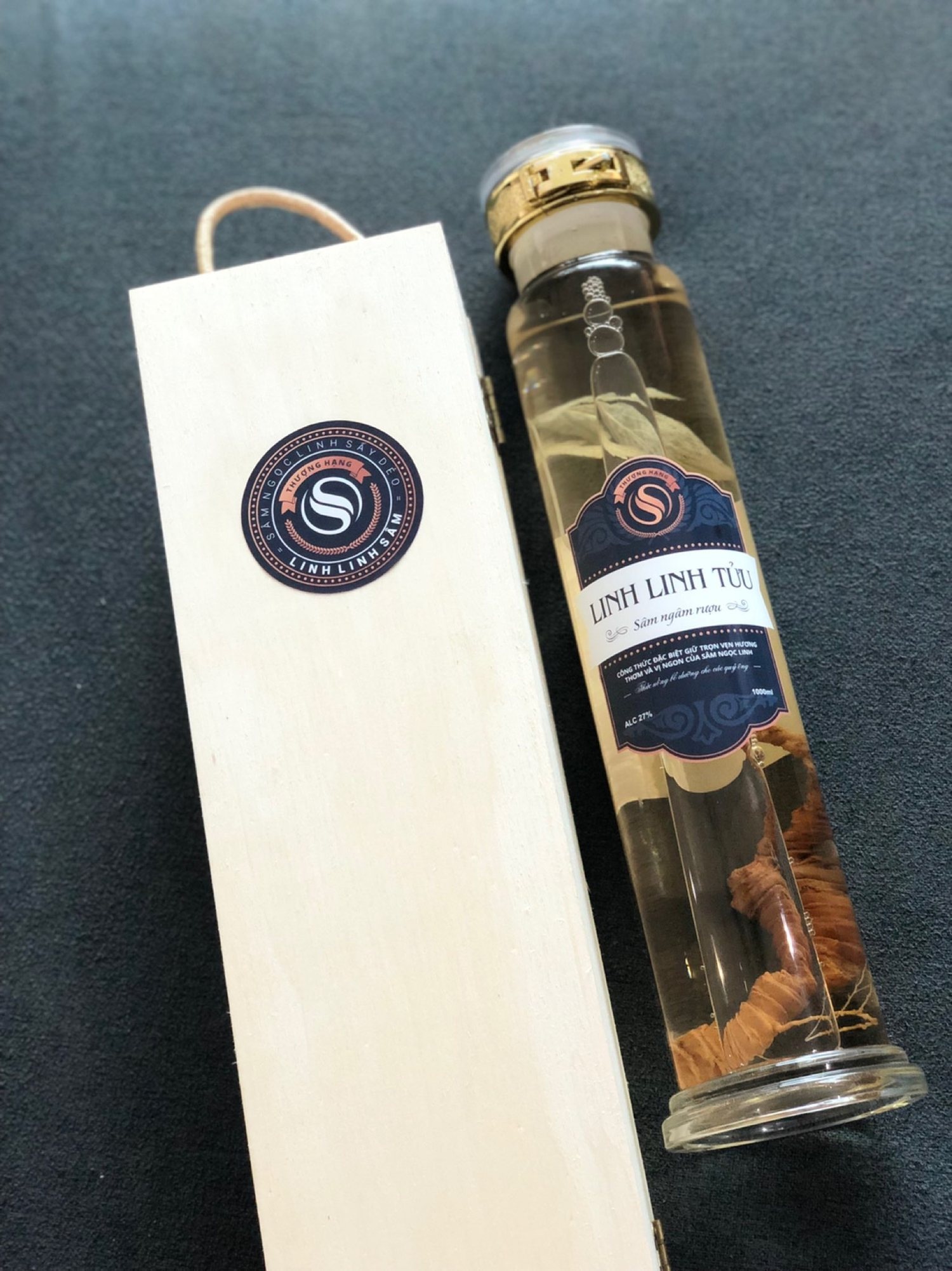 An upright pine box carrying the round LinhLinhSam mark, with the Linh Linh Tửu bottle standing beside it