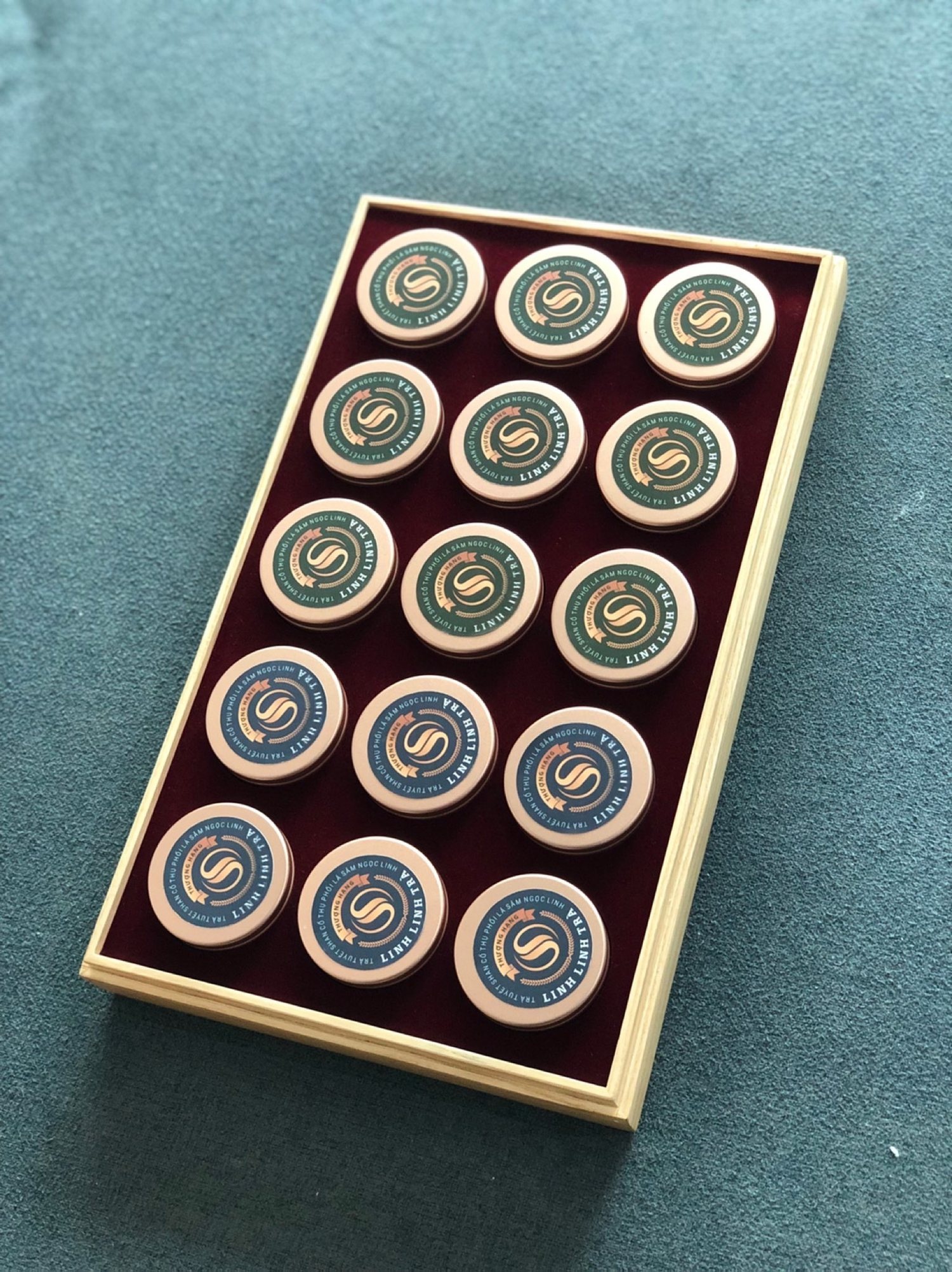 A LinhLinhSam pine box seen from above, fifteen lidded jars set evenly into deep plum velvet