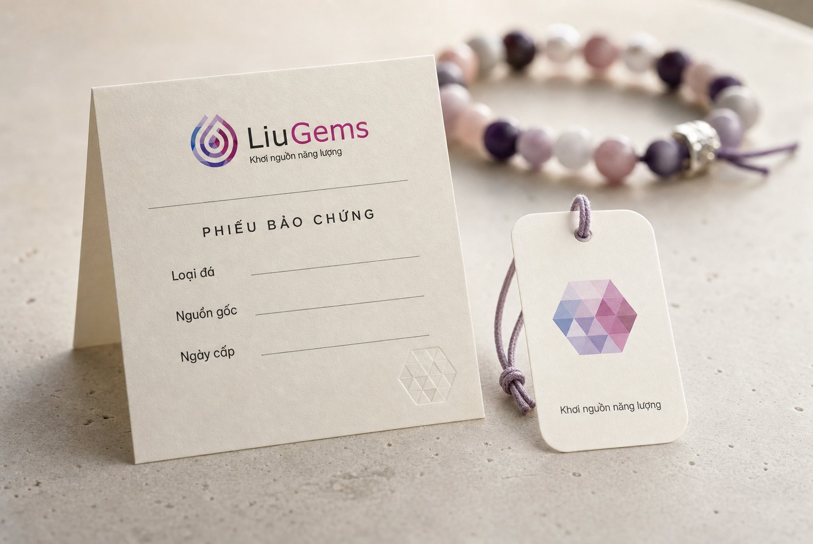 Phiếu bảo chứng LiuGems in trên giấy kem với ba dòng loại đá, nguồn gốc, ngày cấp, đặt cạnh nhãn treo mang hoạ tiết lục giác